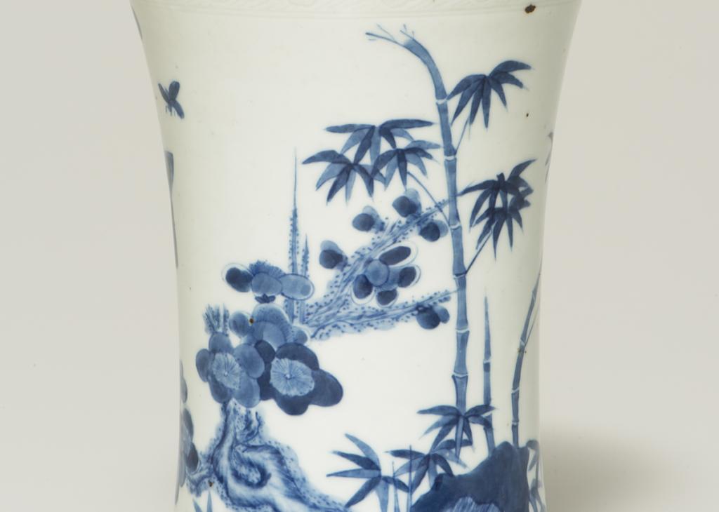 A tall white ceramic pot with bamboo, tress, and flowers painted on it in blue 
