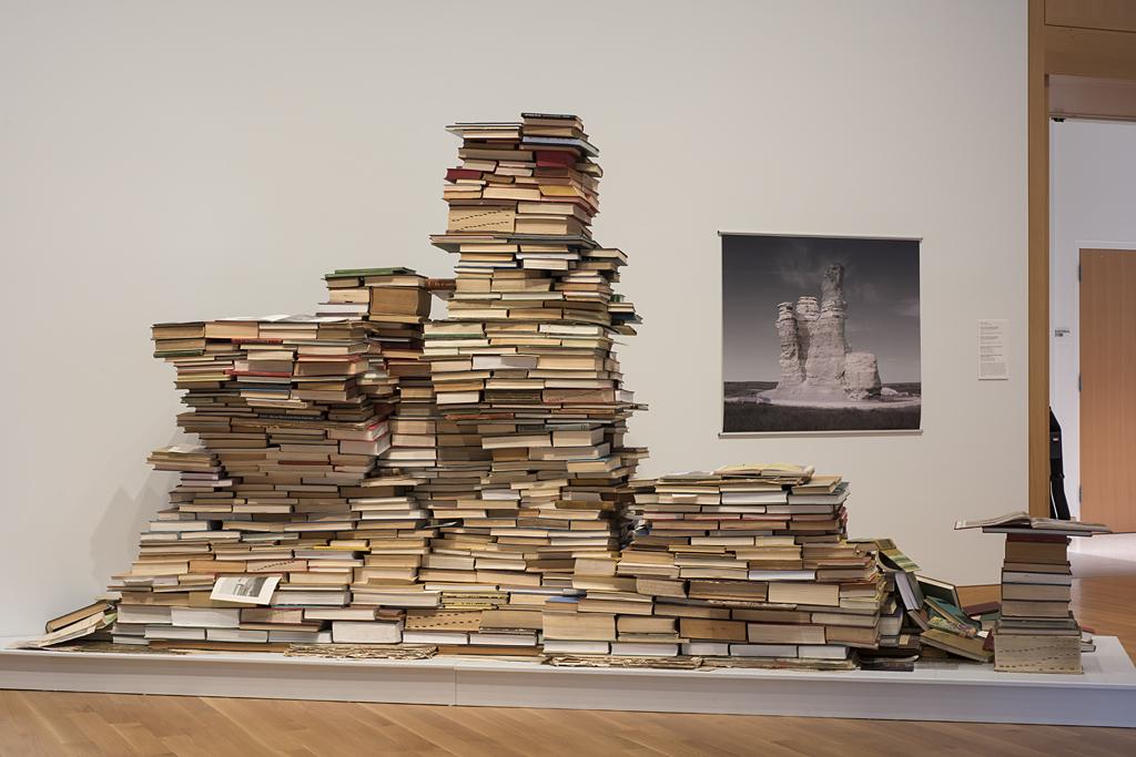 A large pile of books in a gallery stacked artfully on a platform