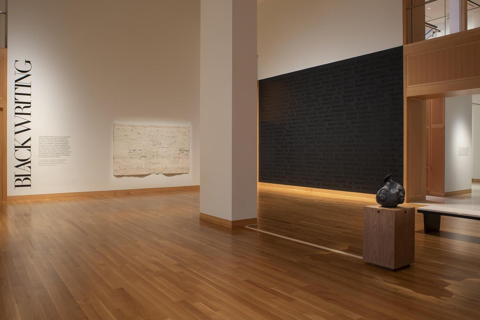 The corner of a gallery space; the text “Black Writing” appears on the left wall; a large black rectangular artwork takes up the right wall   