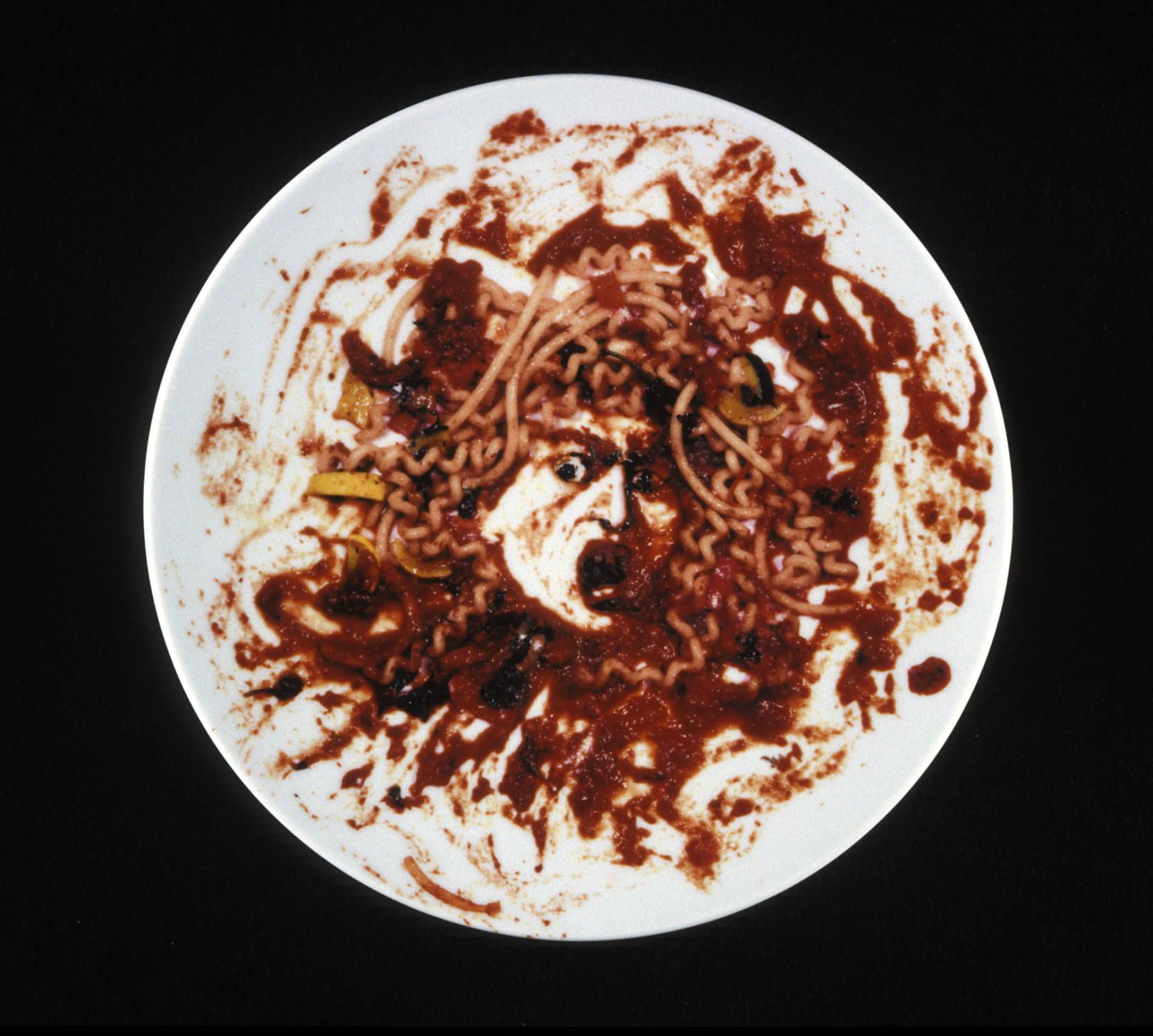 White, flat plate covered in what resembles red pasta sauce with an open-mouthed face in the center 