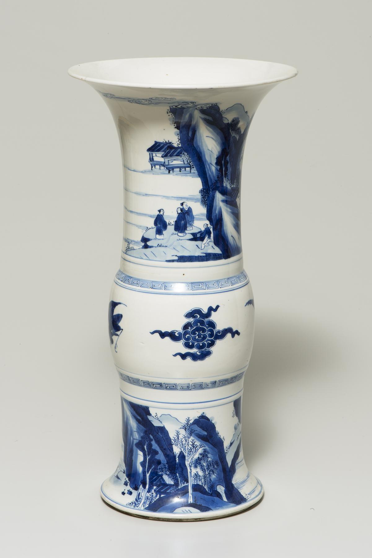 Tall, white vase that flares at top, middle, and bottom decorated in blue with a mountainous landscape at the bottom and several figures conversing on the top
